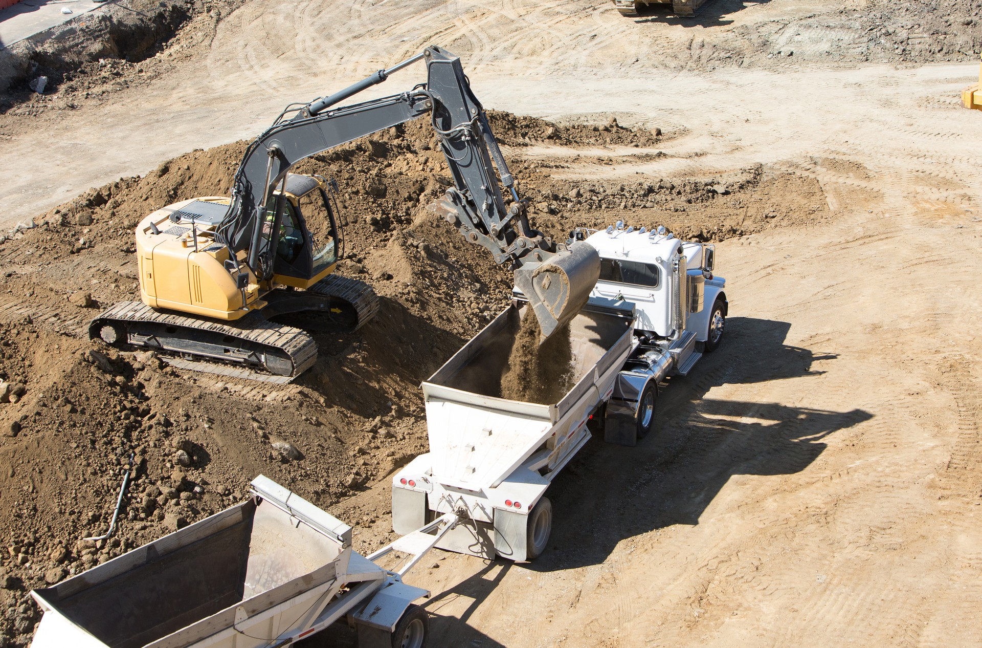 Construction site with excavator loading soil into dirt hauler truck trailer (dump truck)